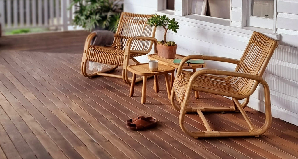 Two sculptural outdoor lounge chairs with teak side tables on a veranda
