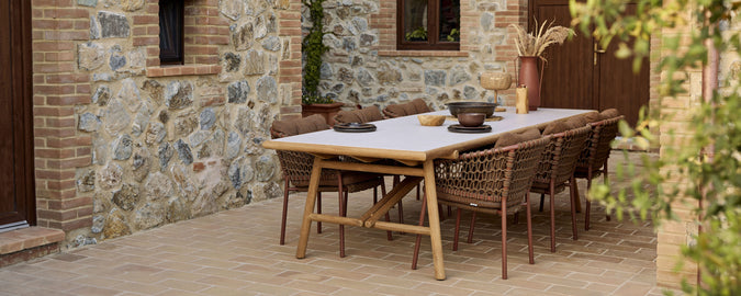 Een houten eettafel voorzien van stijlvolle rotanstoelen, versierd met een decoratieve schaal en een minimalistische tafelopstelling.