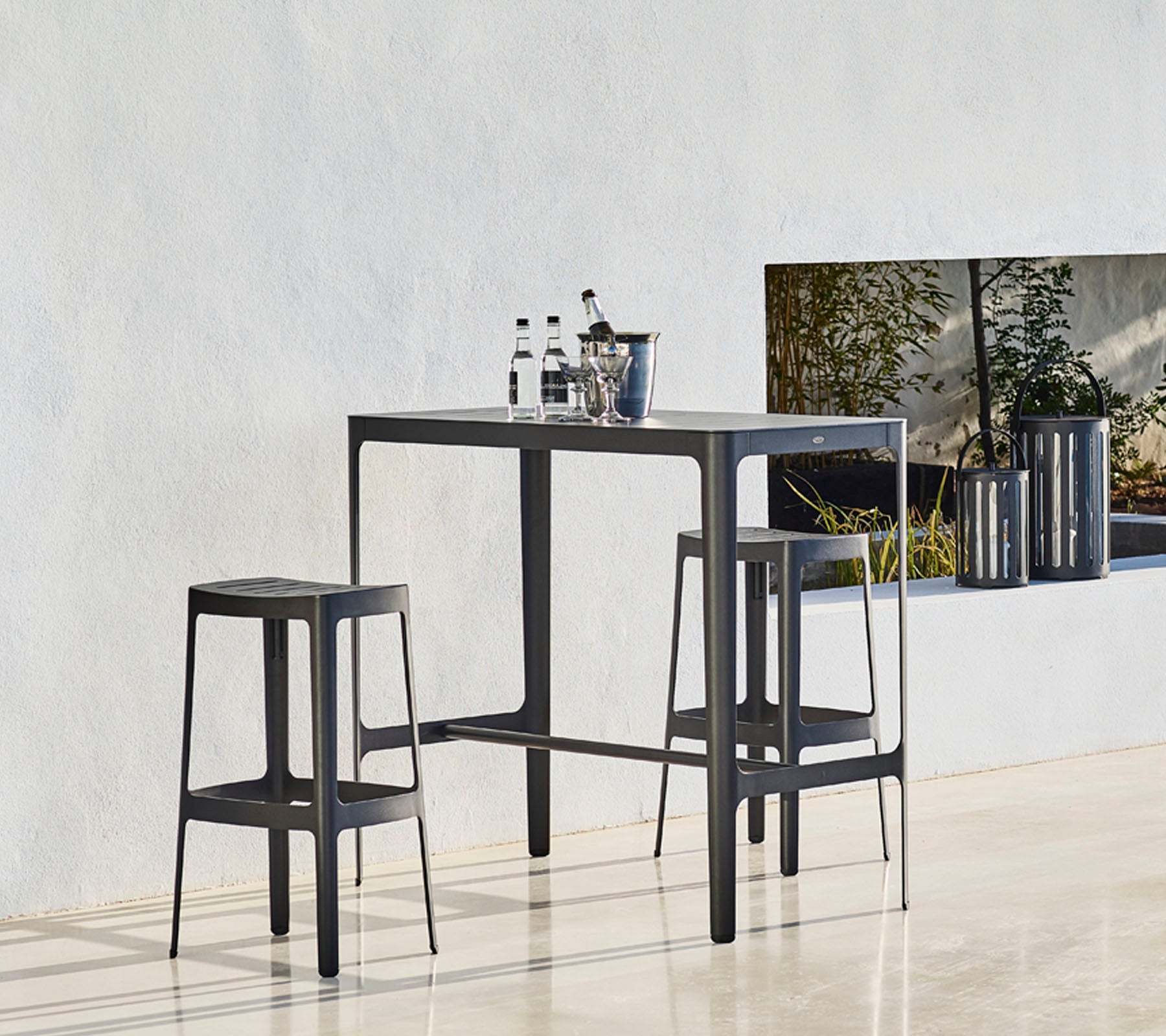 Een afgemaakte tafel met twee bijpassende krukken, met een minimalistisch ontwerp en flessen bovenop, tegen een neutrale achtergrond.