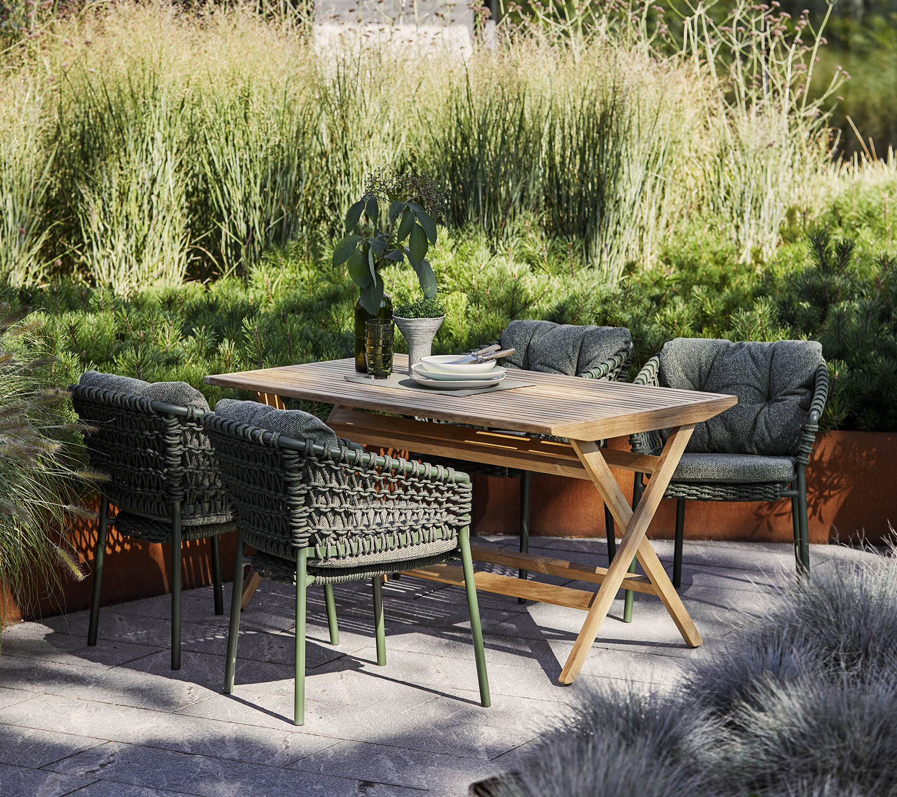 Een stijlvol buitentafelsysteem met een houten tafel en vier gevlochten stoelen, omringd door weelderig groen en decoratieve planten.