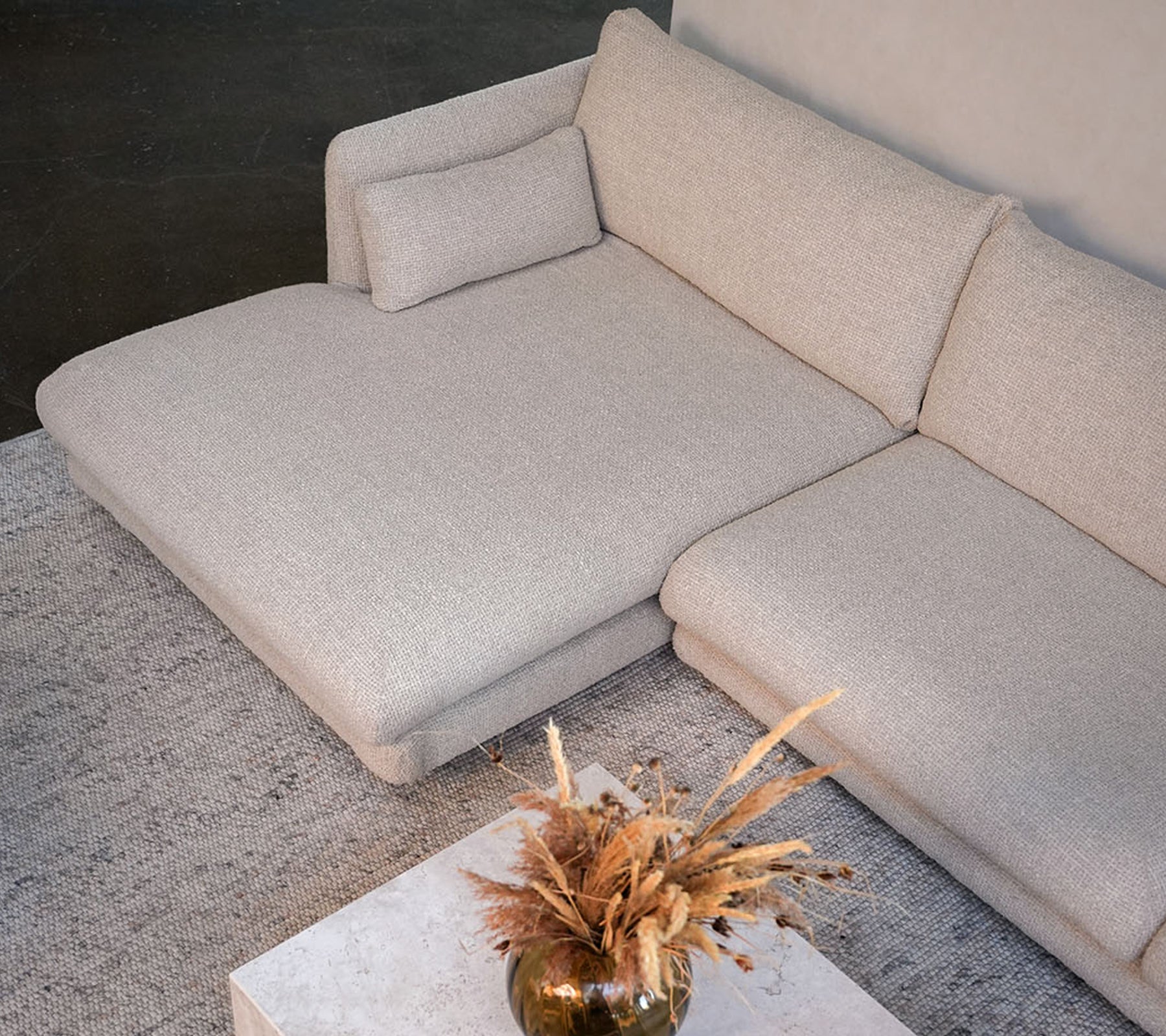 Moderne beige bank met een witte tafel en een decoratieve vaas in een stijlvolle lounge-setting.