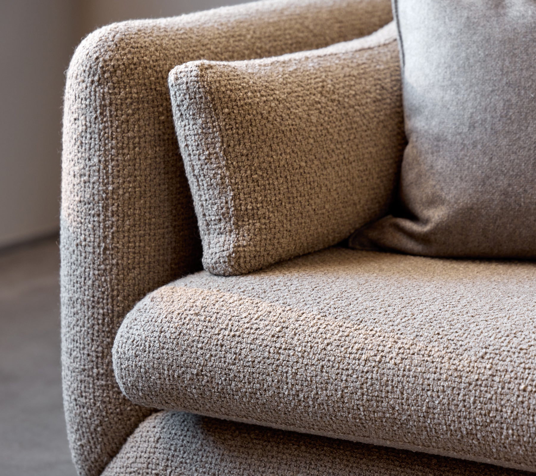 Close-up van een taupe Bloom-sofa armleuning, die de textuur van de stof en het zachte kussen voor extra comfort toont.