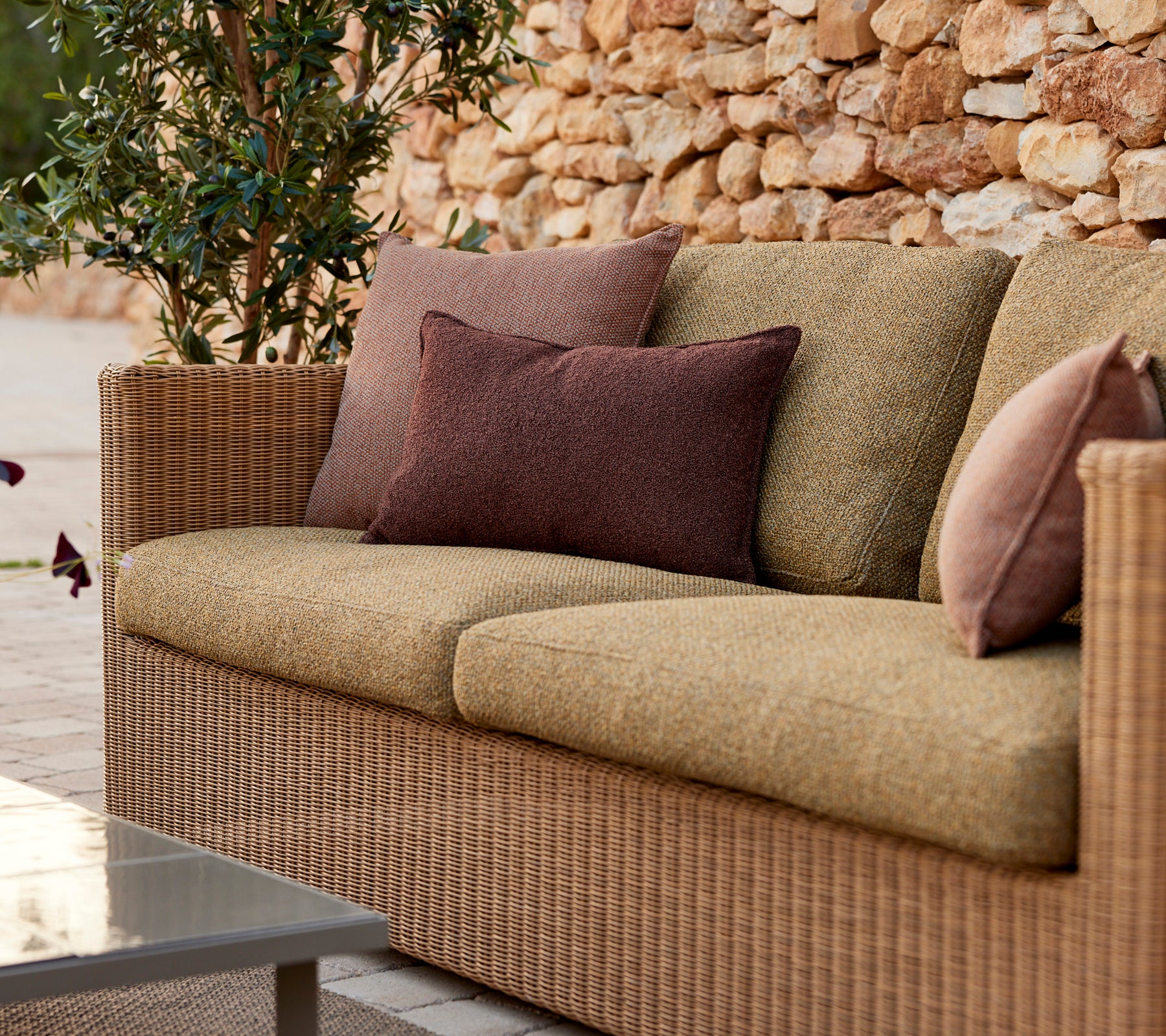 Moderne beige bank met paarse en bruine kussens in een lounge-setting.