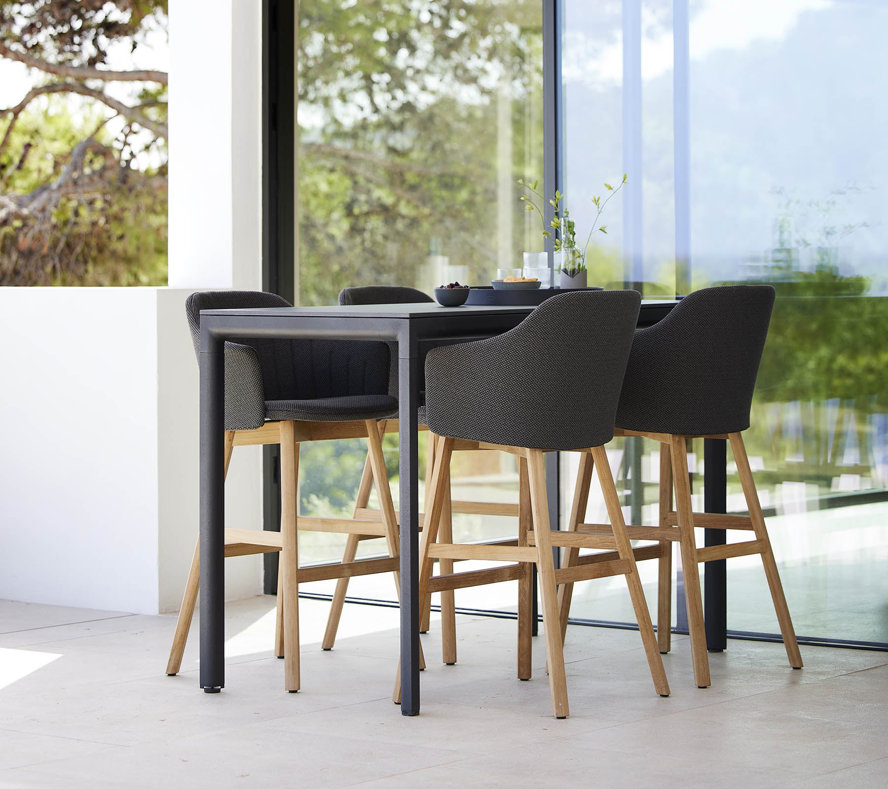 Een stijlvolle drop bar tafel vergezeld van vier moderne barkrukken met houten poten en beklede zittingen.