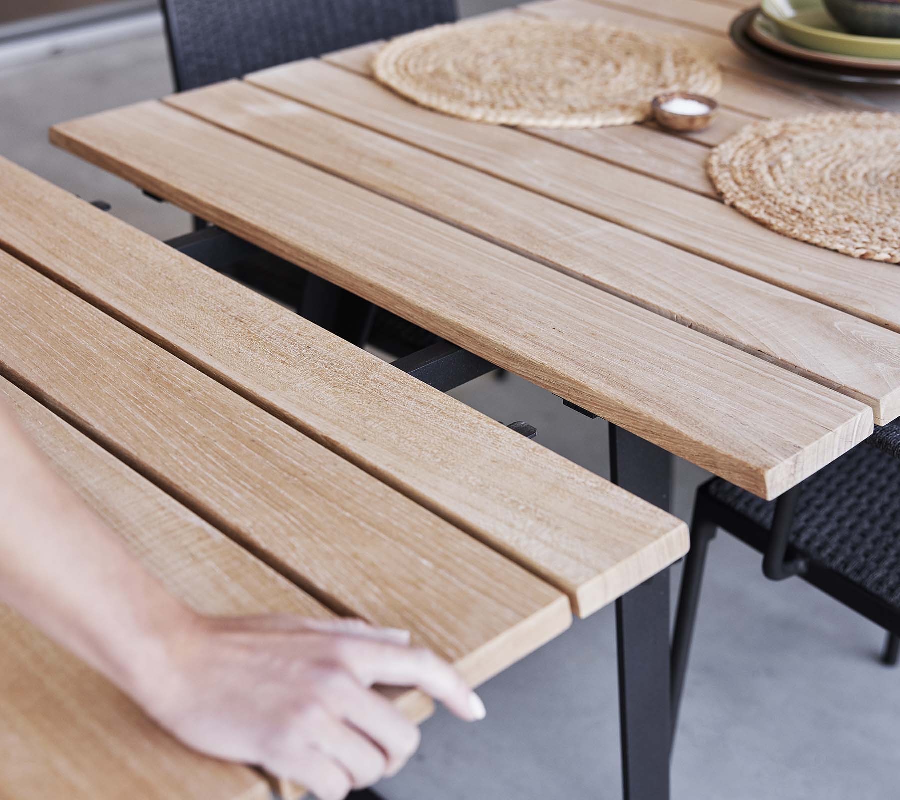 Detail van een houten tafel met lamellenontwerp, placemats en een minimalistische esthetiek, perfect voor dineren of bijeenkomsten.