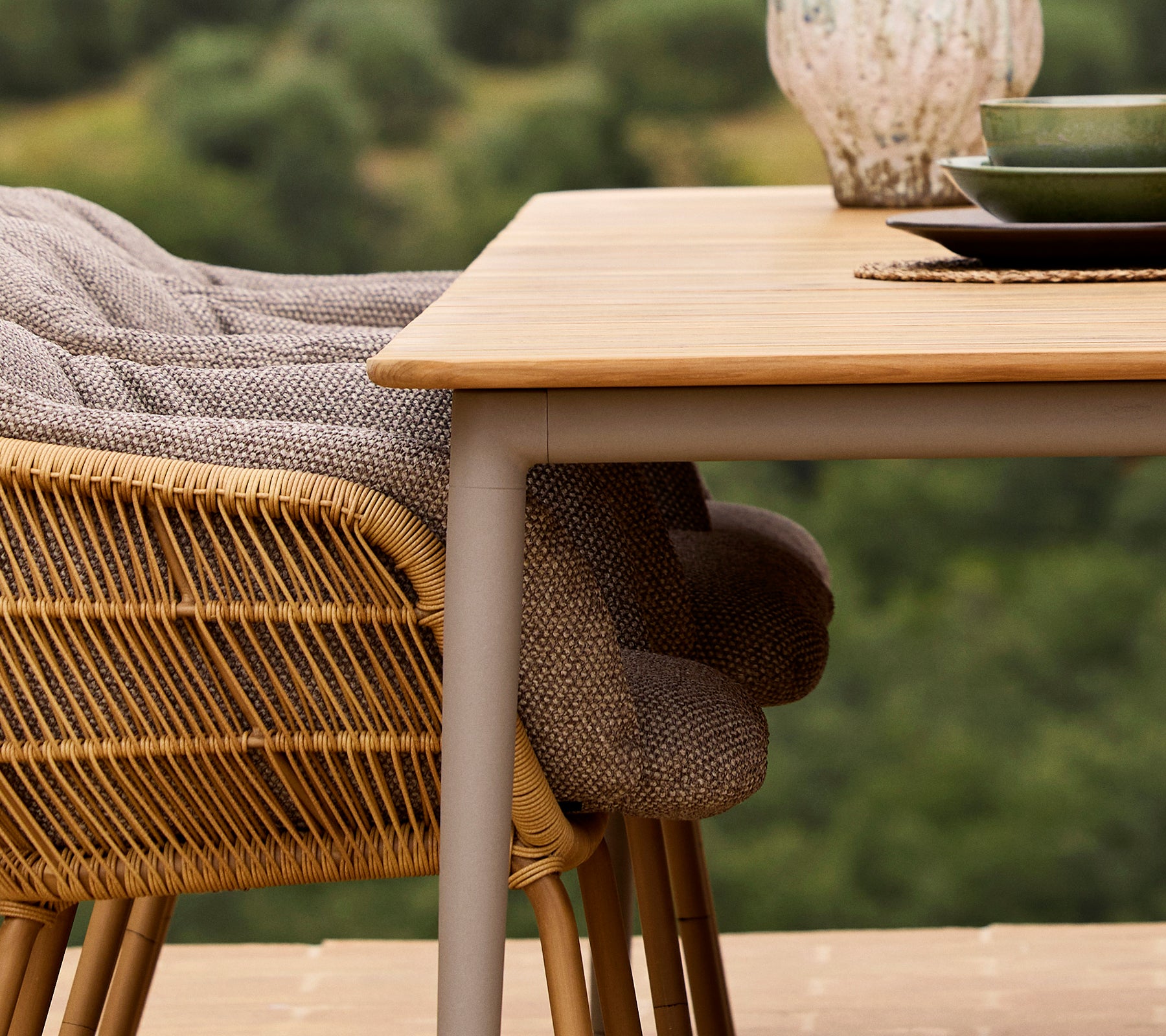 Een close-up van een Core eettafel met een Stay-stoel, voorzien van geweven stof en een groen bord tegen een natuurb backdrop.