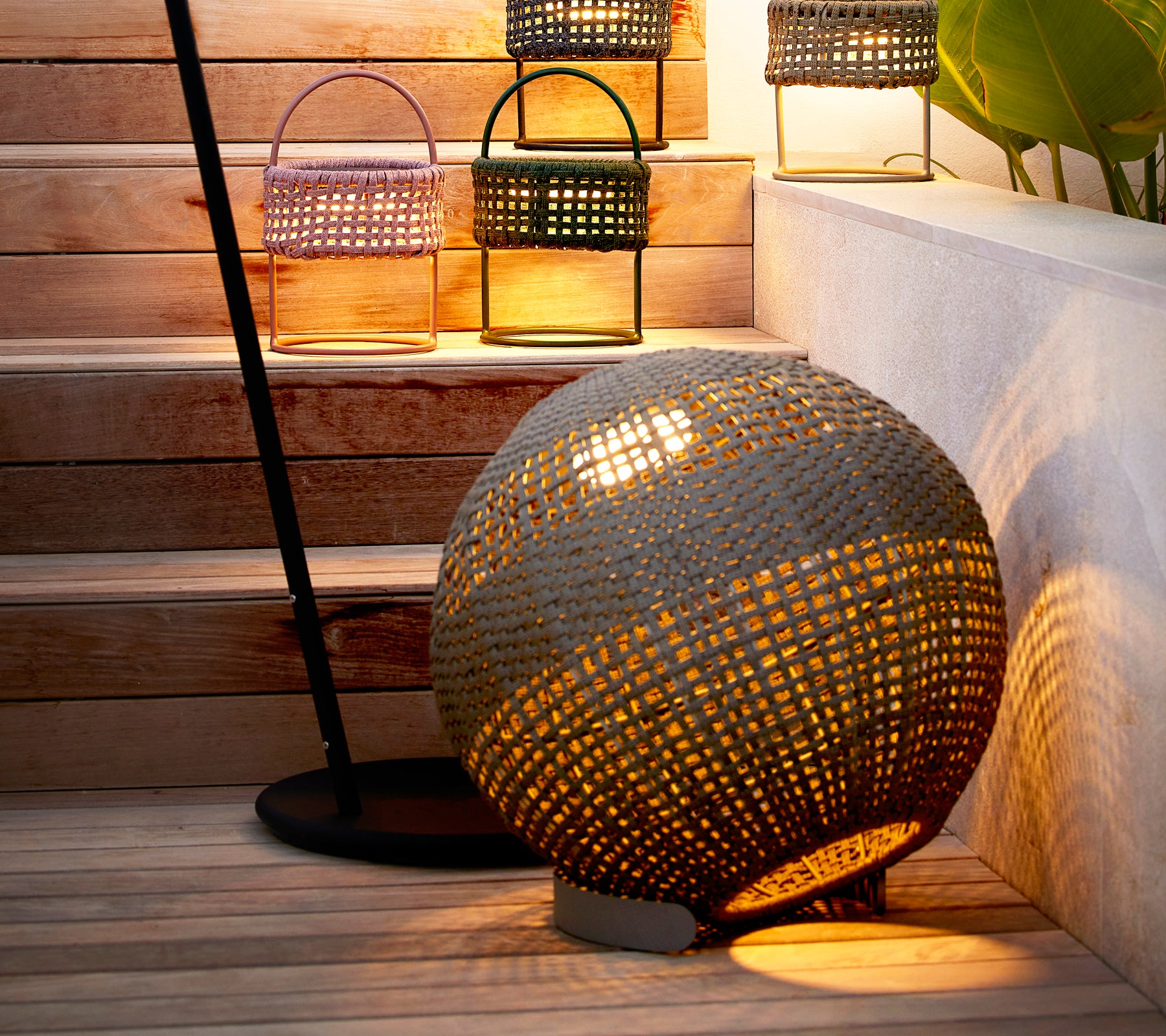 Ronde taupe illusielamp met een geweven design, dat een warme gloed werpt naast stijlvolle lantaarns op een trap.
