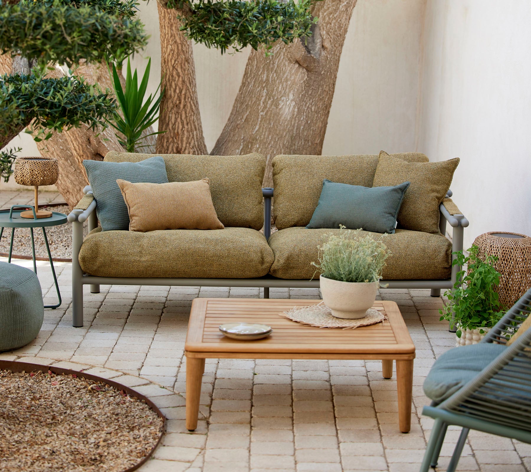 Gewone zithoek met een groene bank met kussens, een houten salontafel en decoratieve planten in een serene omgeving.