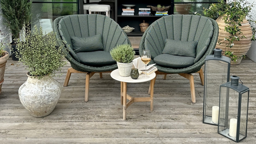 Outdoor shell shaped lounge chairs in dark green with a small round side table and lantern on the side
