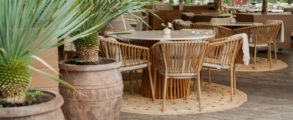 Josefina Restaurant interieur met ronde tafel en natuurlijke Cane-line Ocean stoelen met palmen decor aan de linkerkant