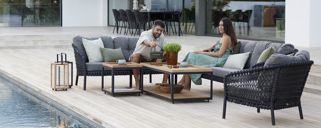 A couple enjoys conversation on a cozy seating arrangement with cushions and a decorative plant on a coffee table.