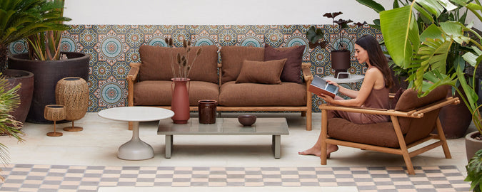 Een gezellige zithoek met bruine loungebanken, een salontafel, planten en decoratieve wandtegels die een ontspannen sfeer creëren.