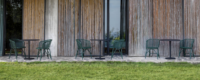 Groene stoelen en zwarte tafels buiten tegen een houten muur geplaatst.