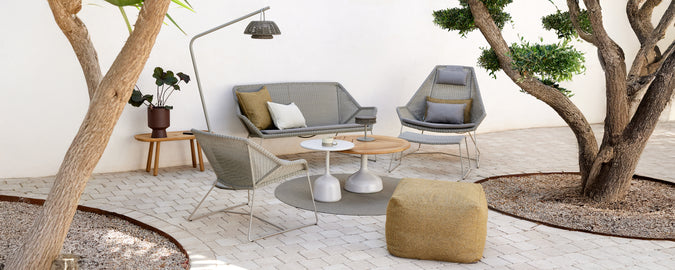 Moderne lounge-instelling met een grijze bank, een grijze stoel, een houten salontafel en een gele poef.