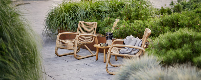 Bohemiaans loungebereich met rieten stoelen en een klein tafeltje met een grijze kussen.