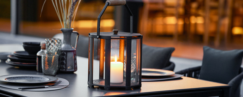 Zwarte lantaarn met kaars en zwart servies op een moderne eettafel.