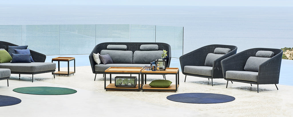 Moderne loungegebied met grijze bank, zwarte fauteuils en houten salontafel.
