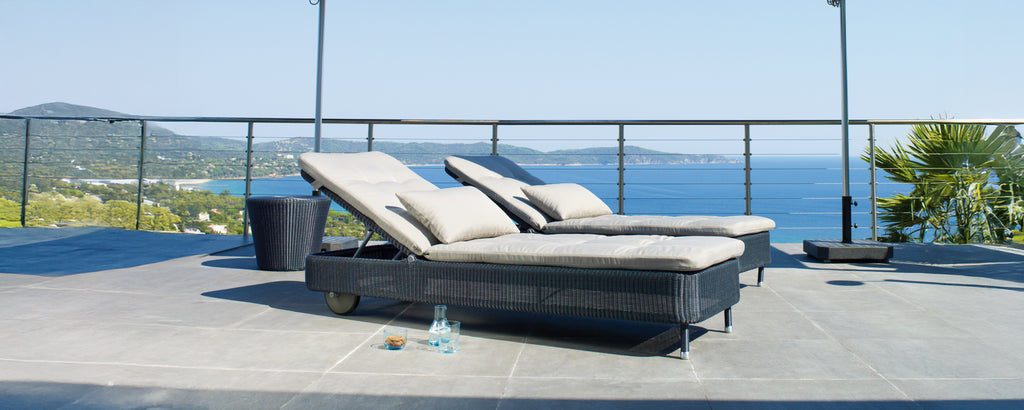 Twee moderne grijze en zwarte loungestoelen op een terras met uitzicht op de oceaan.