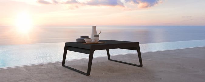 Moderne zwarte tafel op een terras met uitzicht op de zonsondergang boven het water.