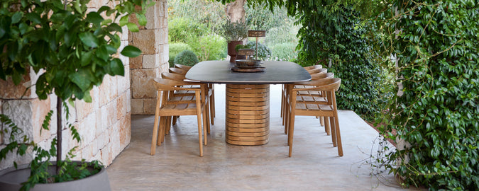 Buiten houten eetstoelen rond een zwarte tafel in een groene tuin.