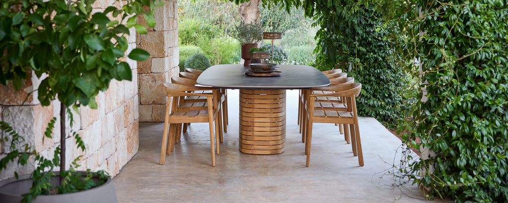 Buiten houten eetstoelen rond een zwarte tafel in een groene tuin.