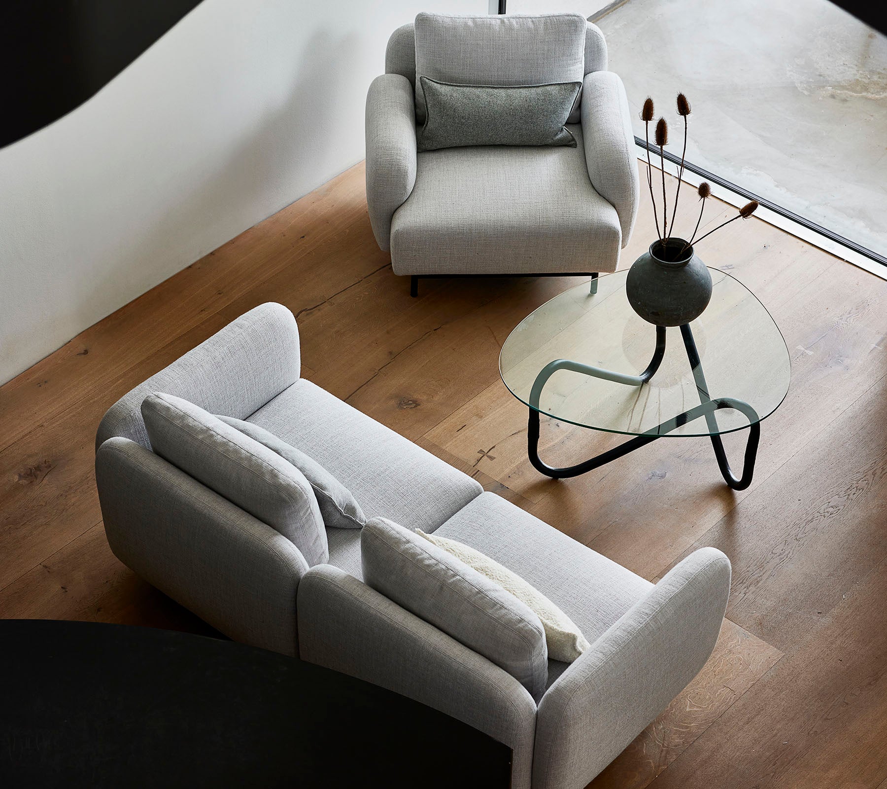 Stijlvolle grijze sofa's en een elegant glazen salontafel met decoratieve elementen op het tafelblad, tegen een warme houten vloer.