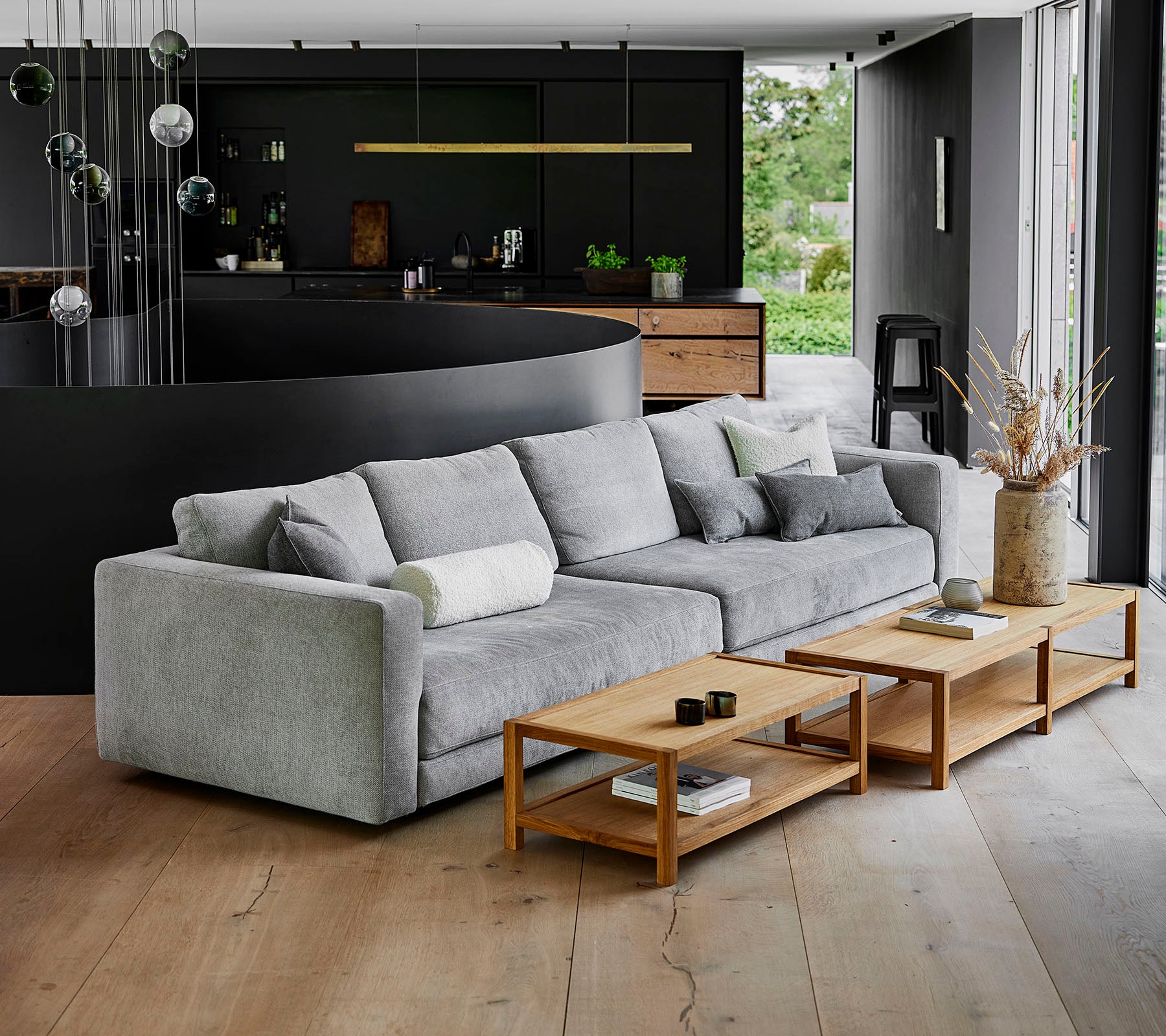 Een moderne, grijze bank met zachte kussens naast houten koffie tafels in een eigentijdse omgeving met stijlvolle decoratie.