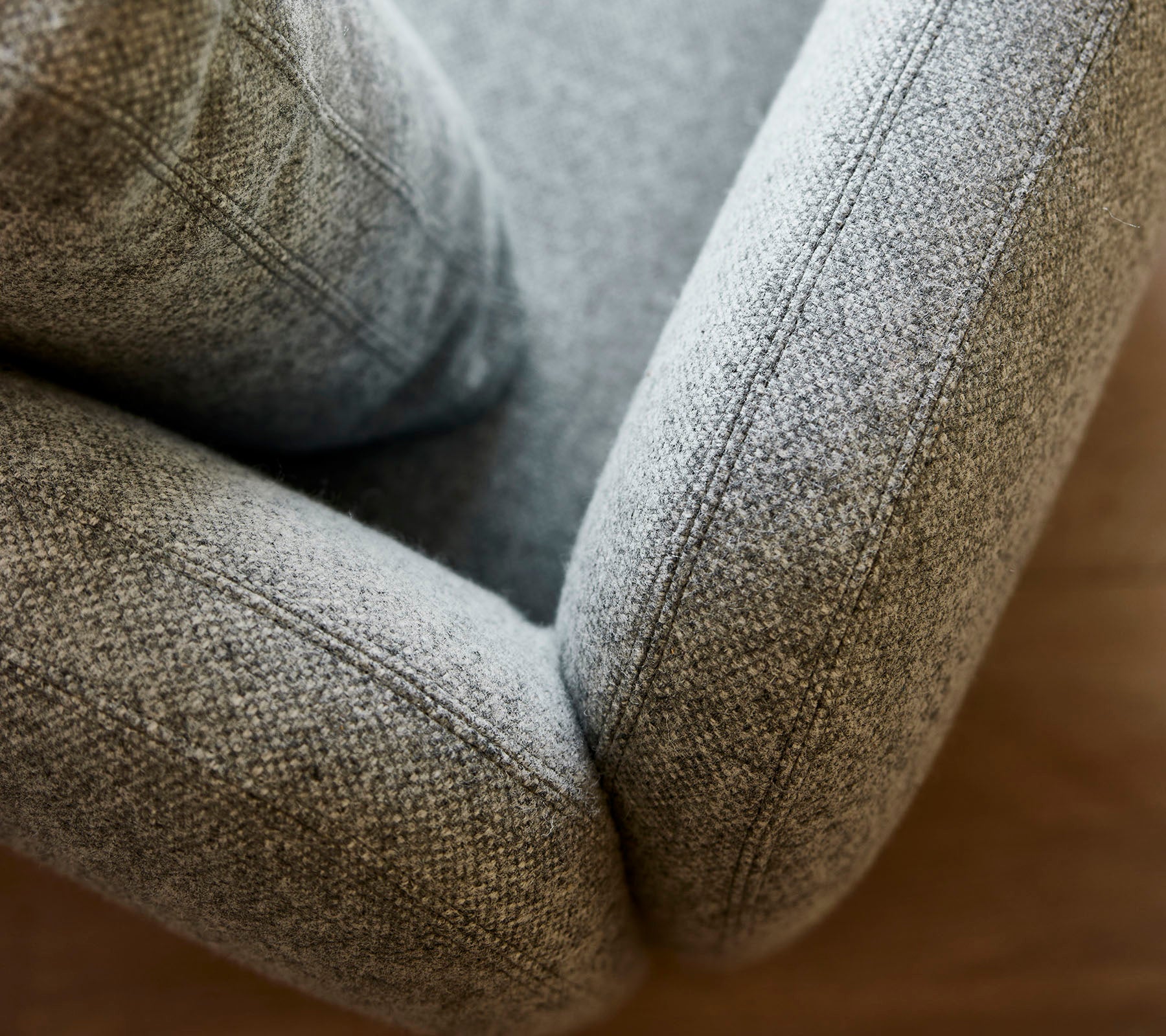 Close-up van een zachte, gestructureerde grijze gestoffeerde fauteuil, die gladde lijnen en gedetailleerde stiksels toont.