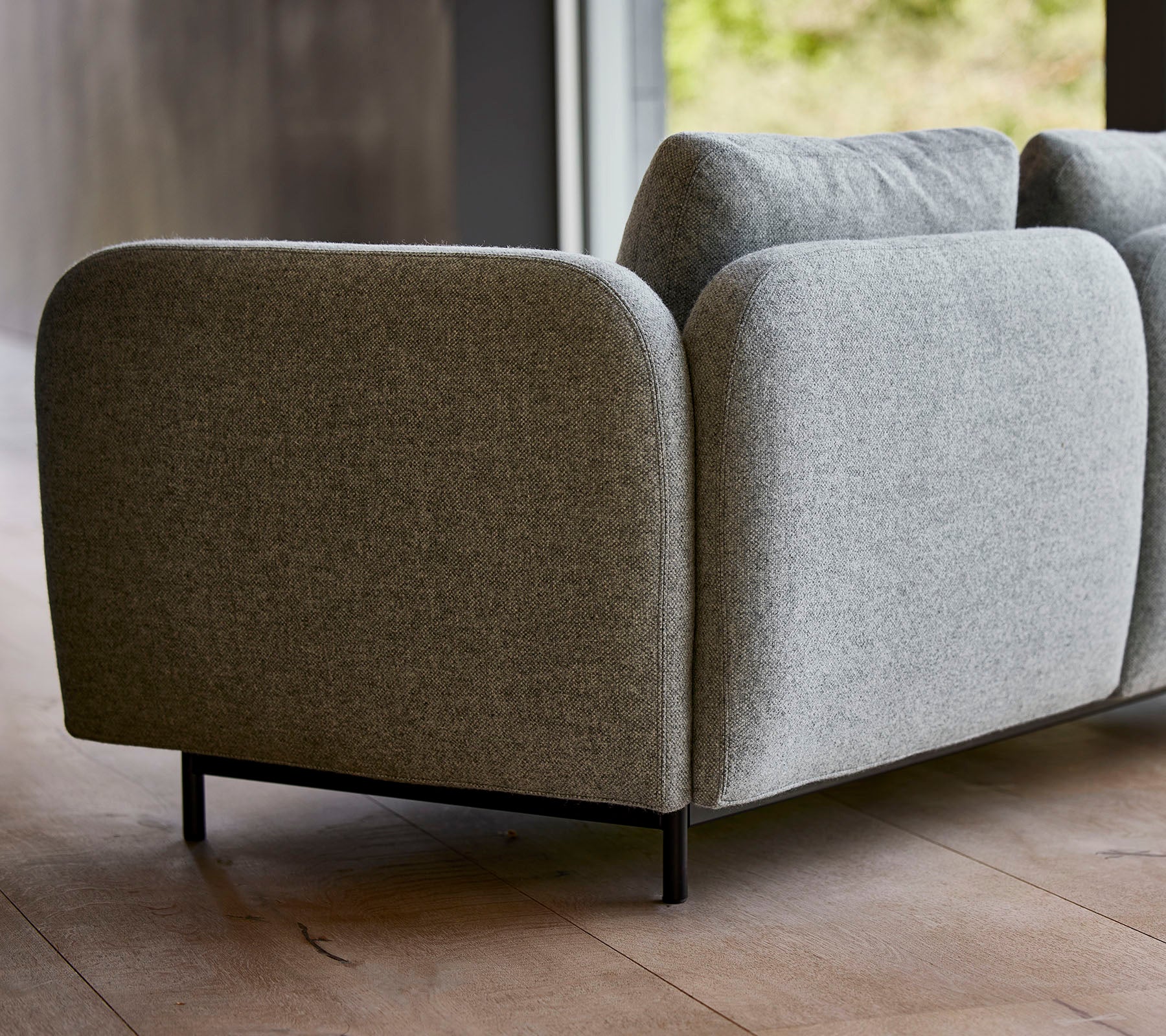 Een moderne grijze gestoffeerde bank met afgeronde hoeken en slanke zwarte poten, die een minimalistisch ontwerp laat zien.