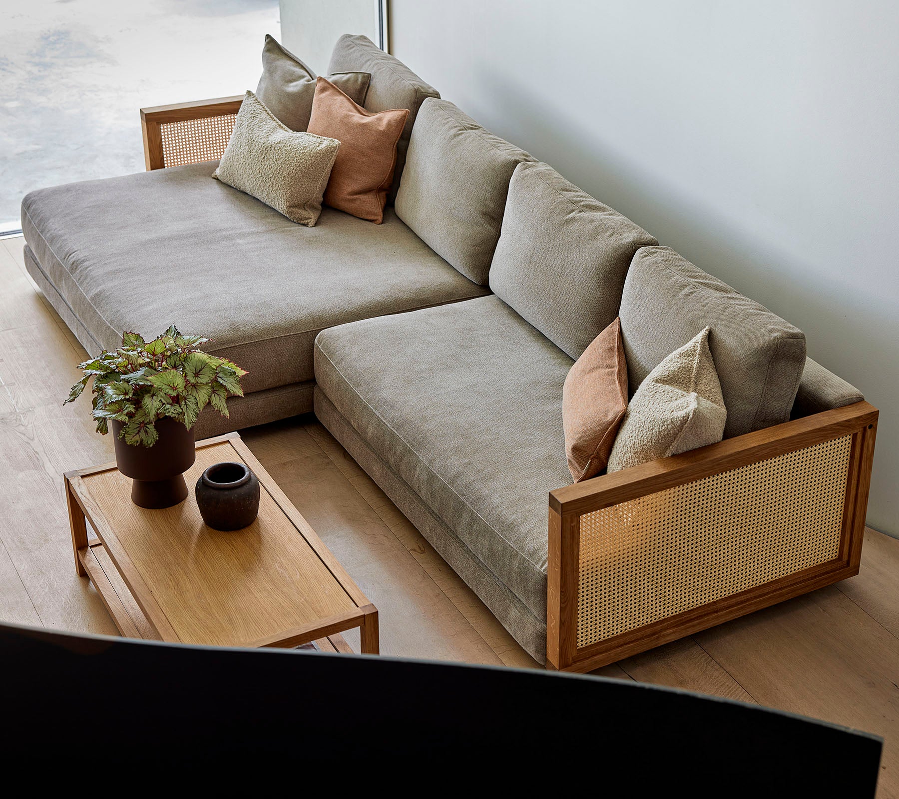 Een stijlvolle hoekbank met zachte kussens en decoratieve kussens, in combinatie met een houten salontafel met planten en elegante decoratie.