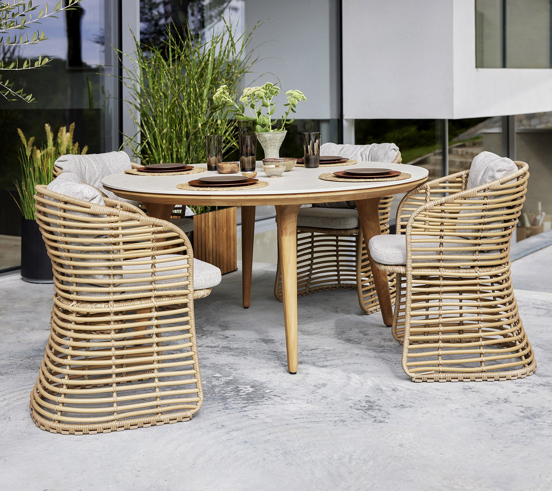 Een ronde tafel met vier een fauteuilstolen, voorzien van kussens, omringd door groen voor een stijlvol eetgedeelte.