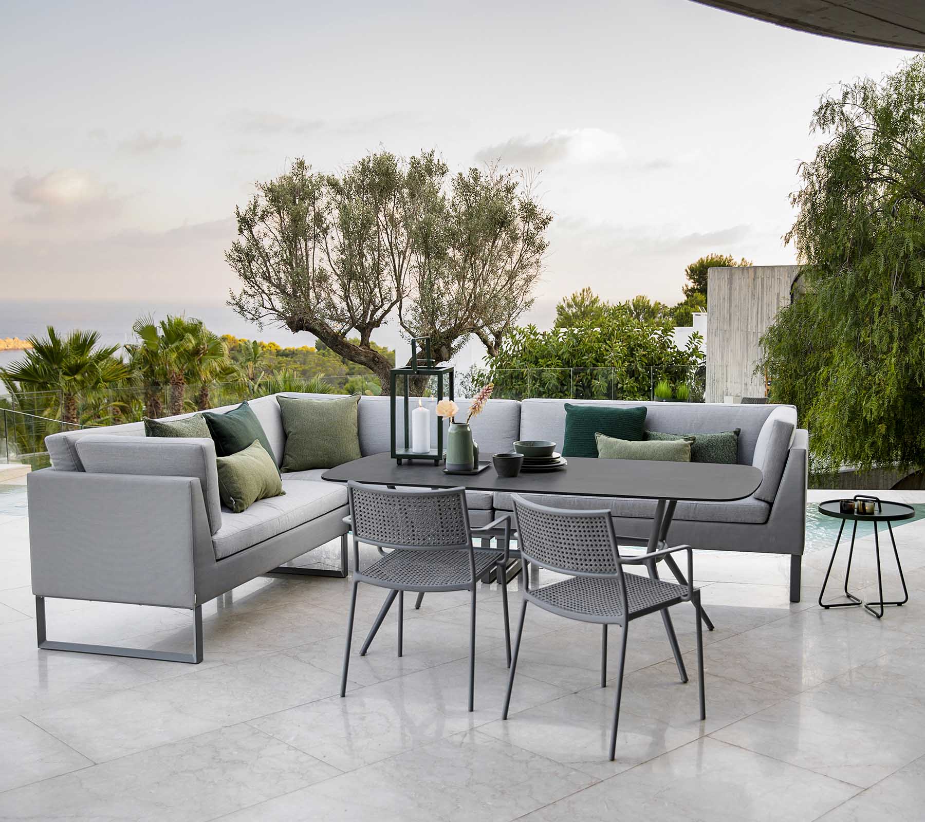 Moderne buitensitgebied met een stijlvolle loungebank, een eettafel en metalen stoelen omgeven door groen.