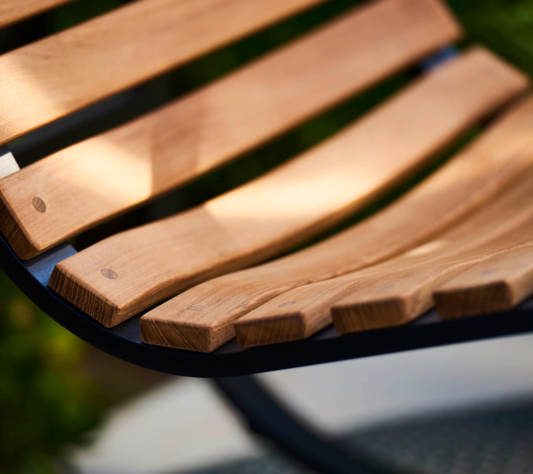 Close-up van een gebogen houten banklat met gladde, natuurlijke houtnerf, die vakmanschap en een warm, uitnodigend ontwerp laat zien.