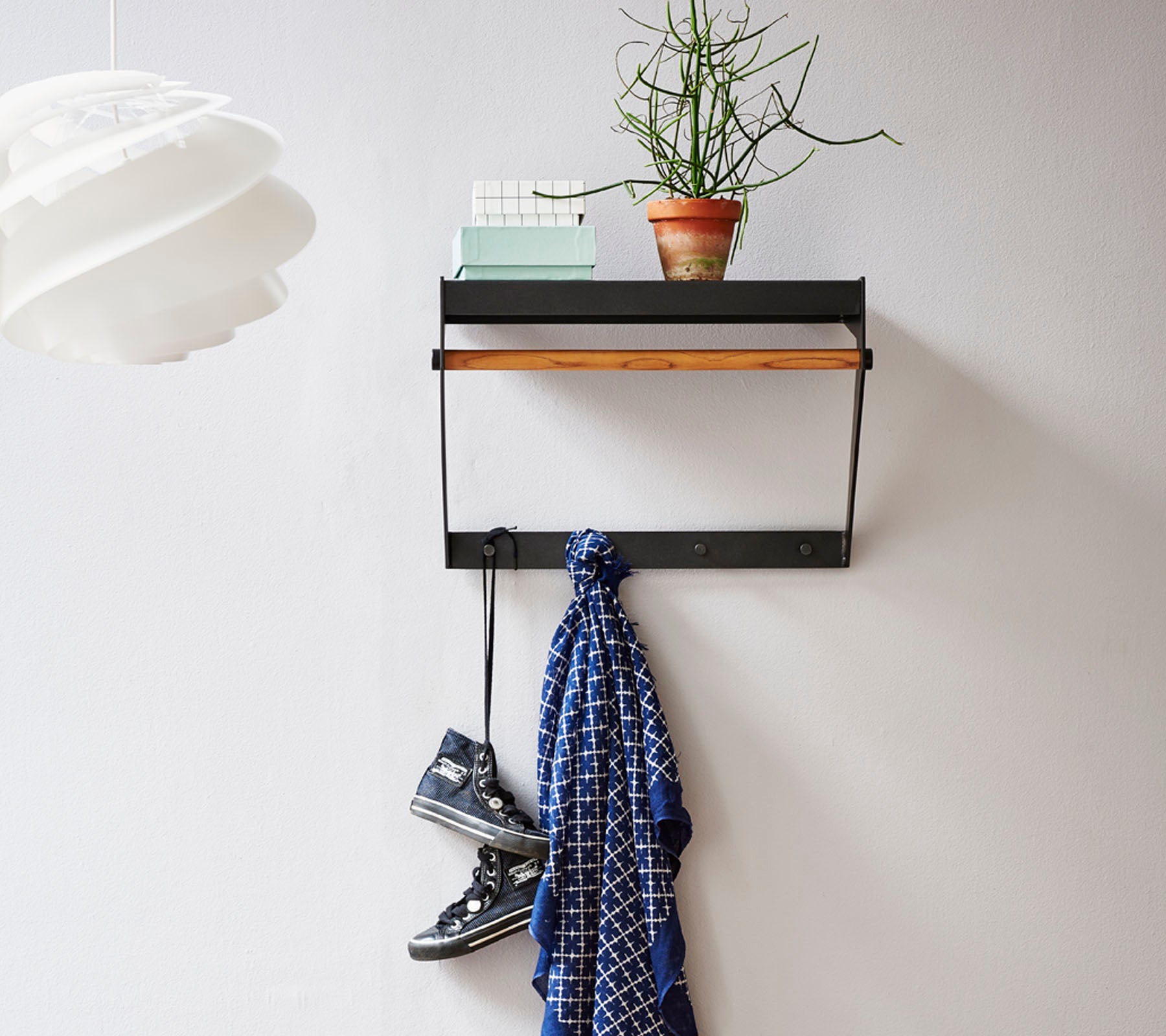 Wandplank met een houten bovenkant, met een kleine plant, een sjaal die daaronder hangt en een paar schoenen op de vloer.