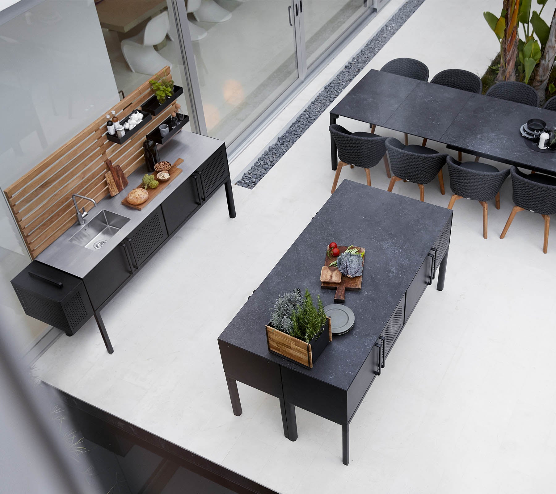 Moderne buitenkeukenopstelling met een slanke aanrecht, een ruime eettafel en stijlvolle zitarrangement met planten en decoratieve elementen.