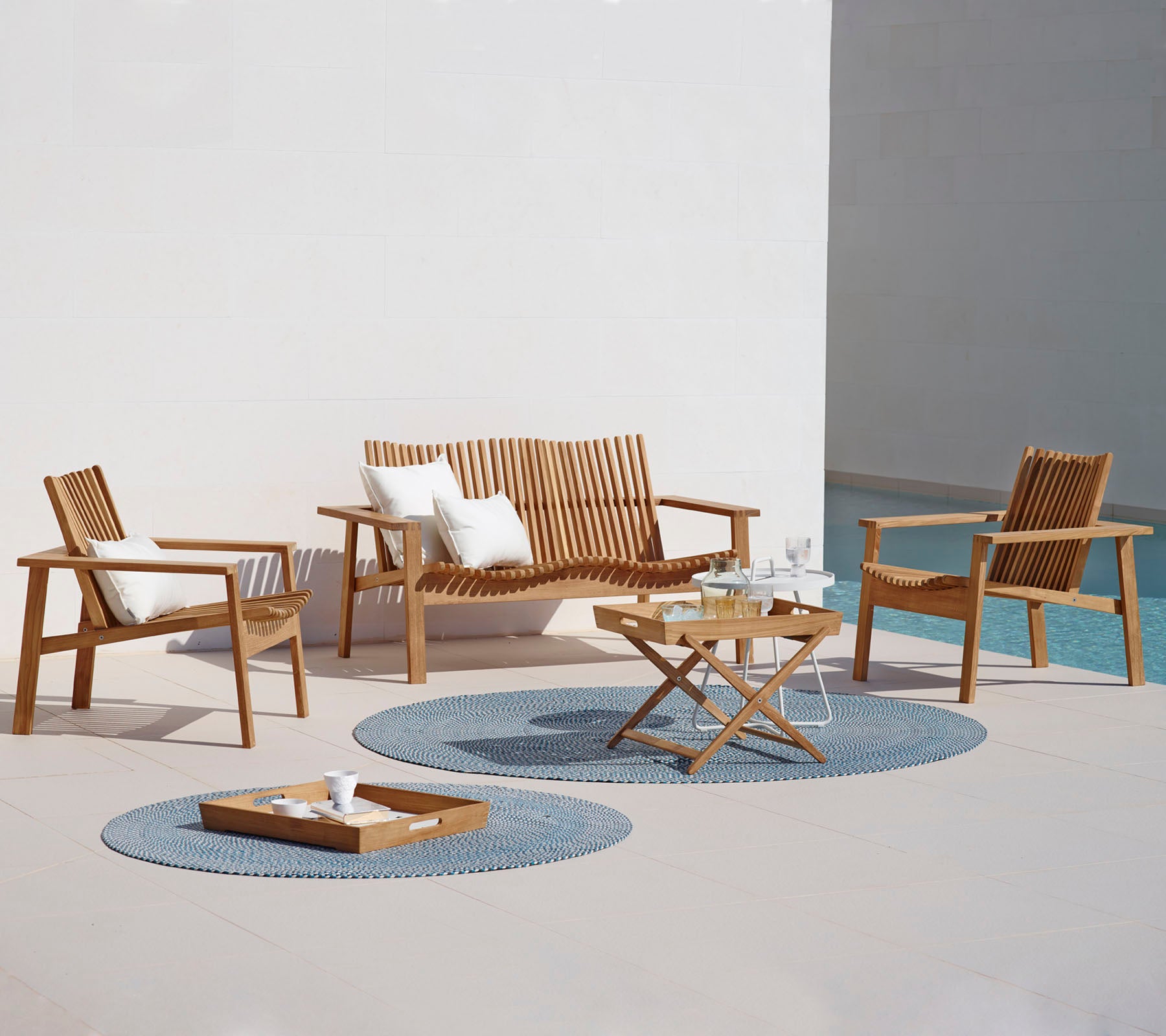 Een stijlvolle buitenzitarrangement met een bank, twee fauteuils, een salontafel en decoratieve tapijten. Ideaal voor ontspanning.
