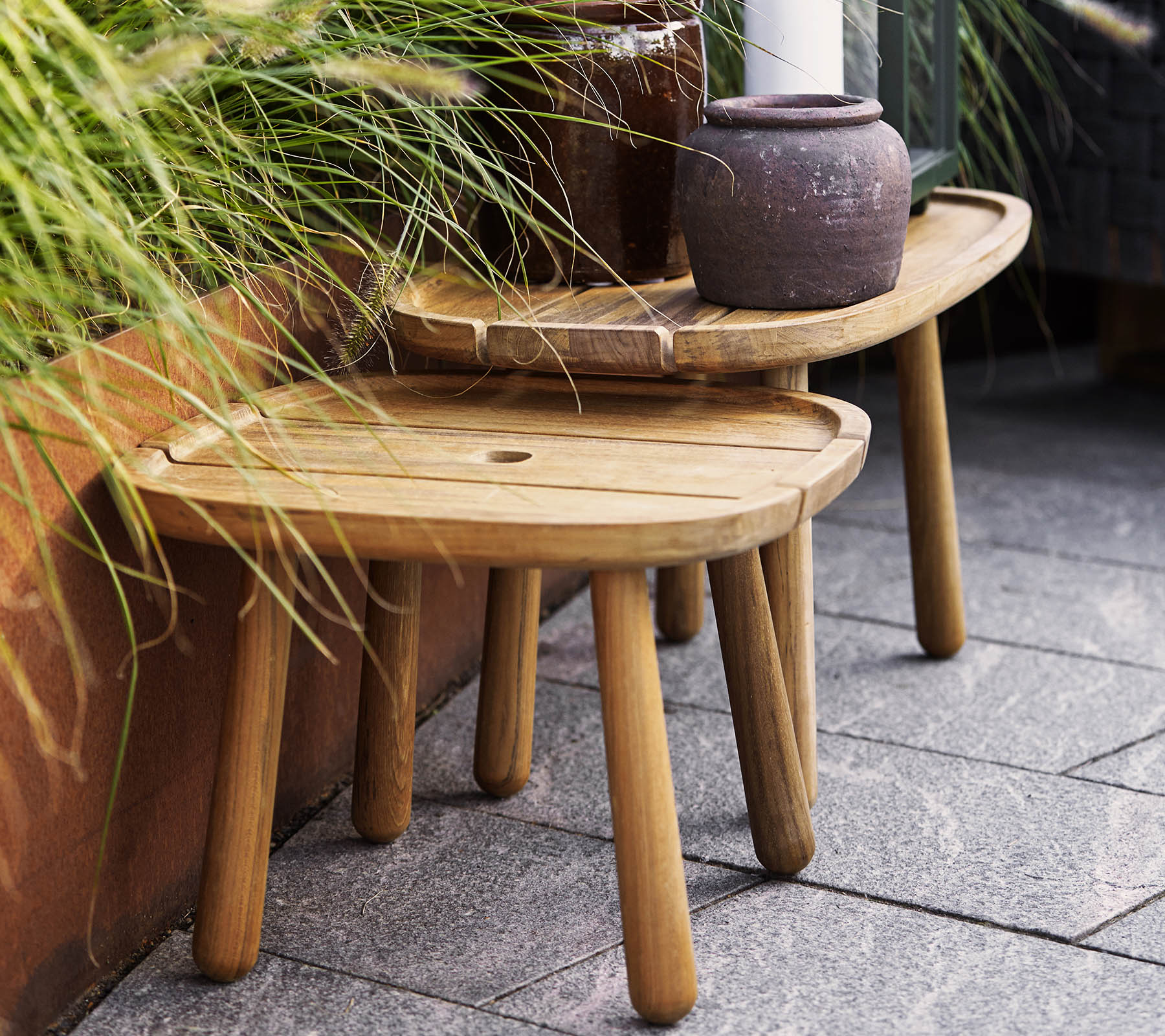 Twee stijlvolle houten krukken in verschillende hoogtes, aangevuld met een keramische pot en groen in de achtergrond. Ideaal voor decoratief gebruik.