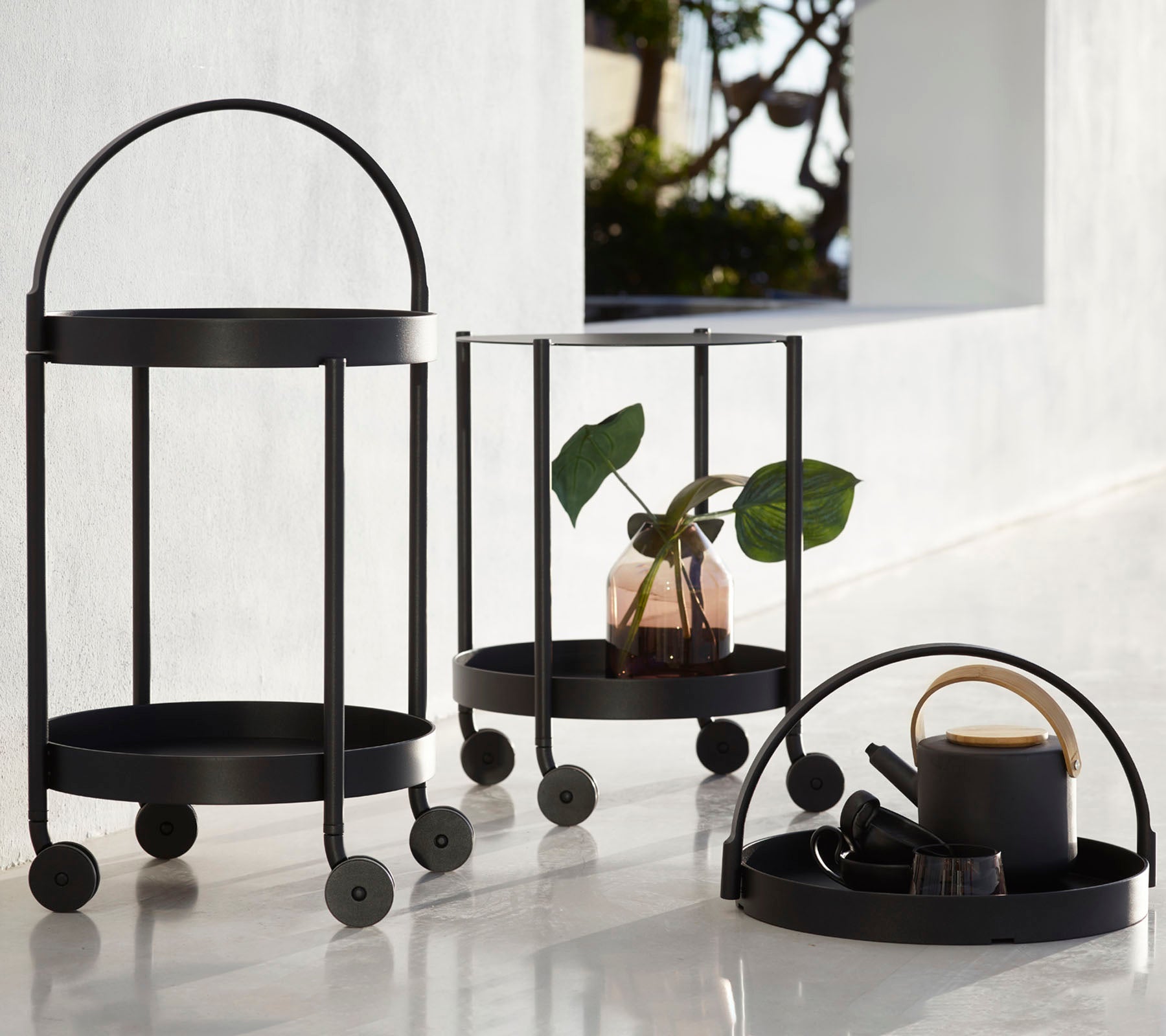 Drie zwarte metalen wagens met ronde frames en wielen, met een plant, decoratieve items en een beker, opgesteld voor vertoning.