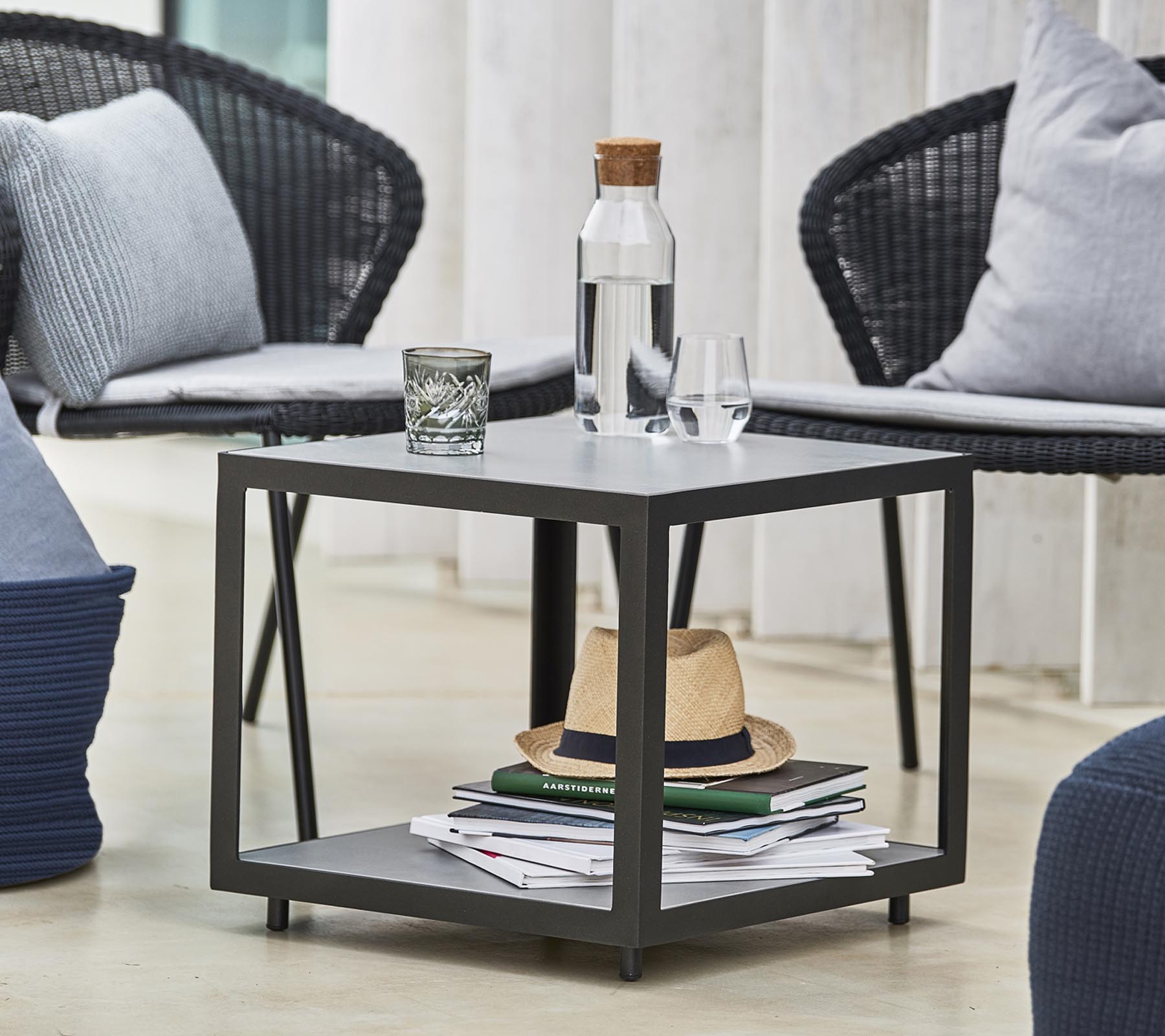 Een moderne tafel met een waterfles, een glas en decoratieve items, omringd door stijlvolle stoelen en kussens.