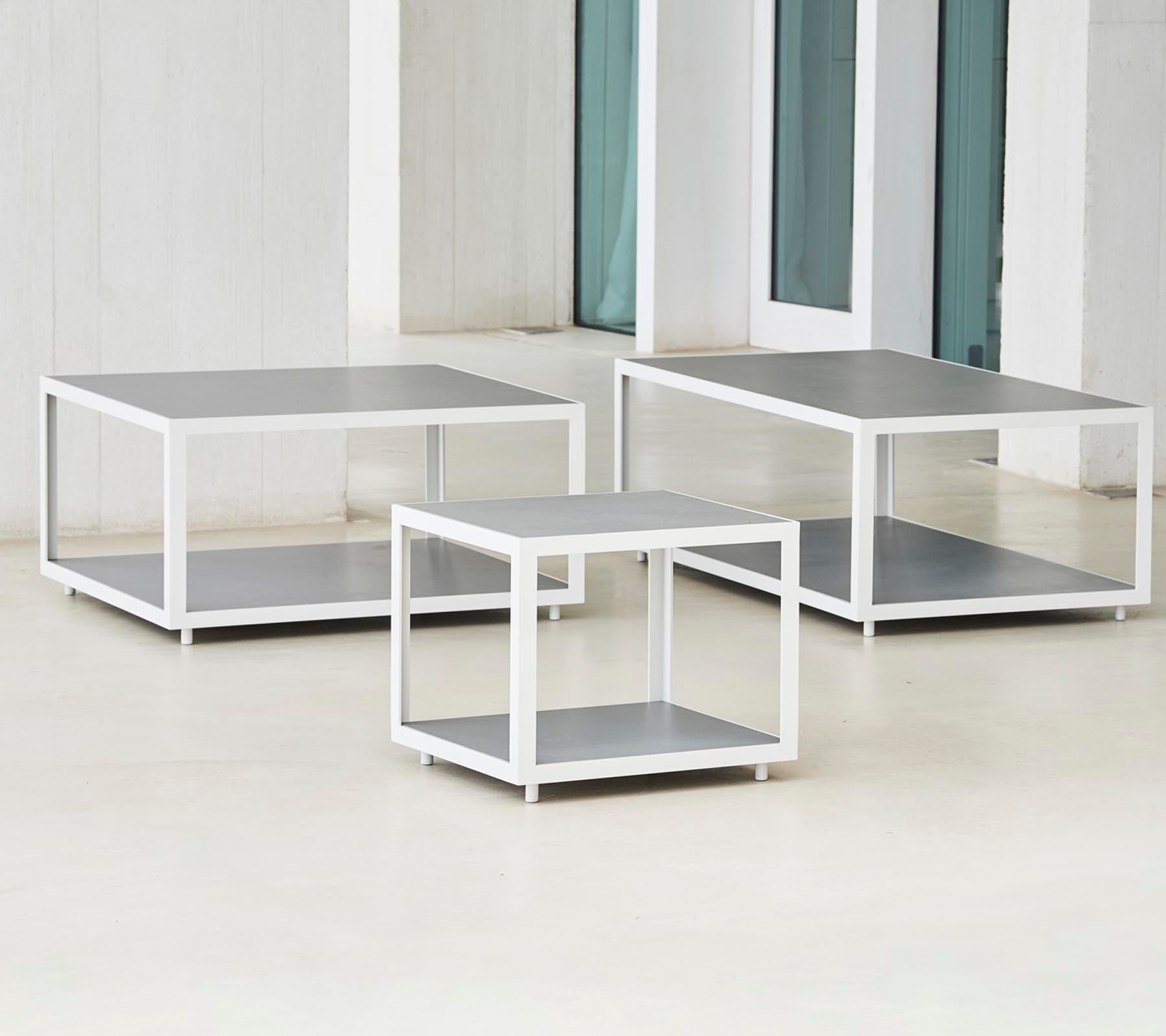 Een set van drie moderne tafels met een strak ontwerp met metalen frames en vlakke oppervlakken, gerangschikt in verschillende maten.
