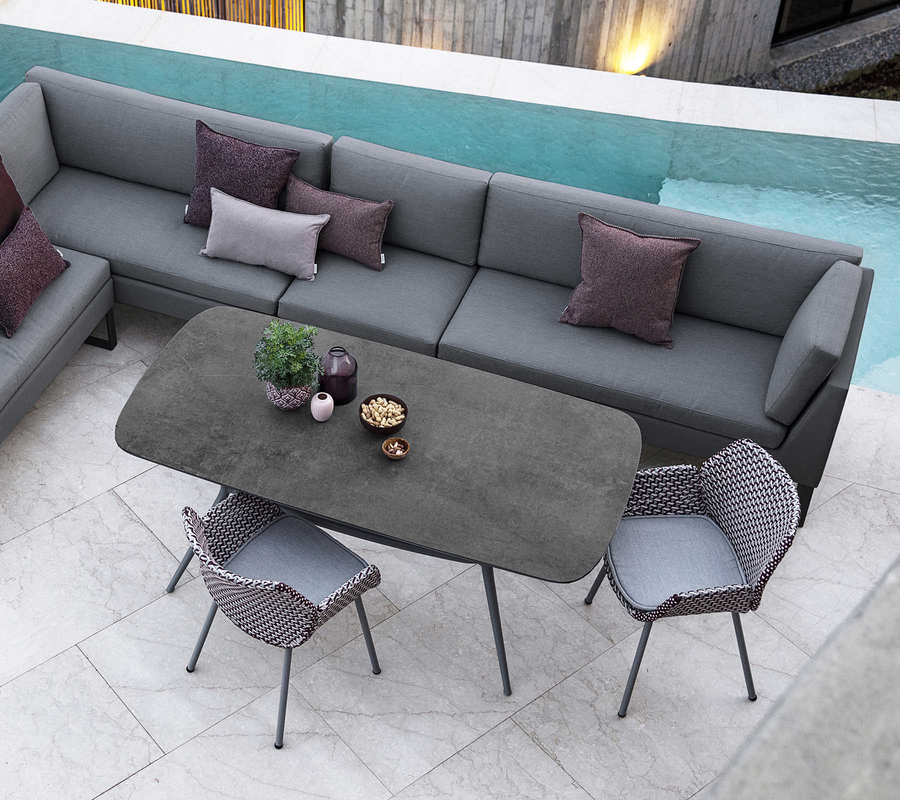 Moderne buitenzitje met een modulebank met kussens, een strak rechthoekig tafel, en stijlvolle stoelen, aangevuld met uitzicht op het zwembad.