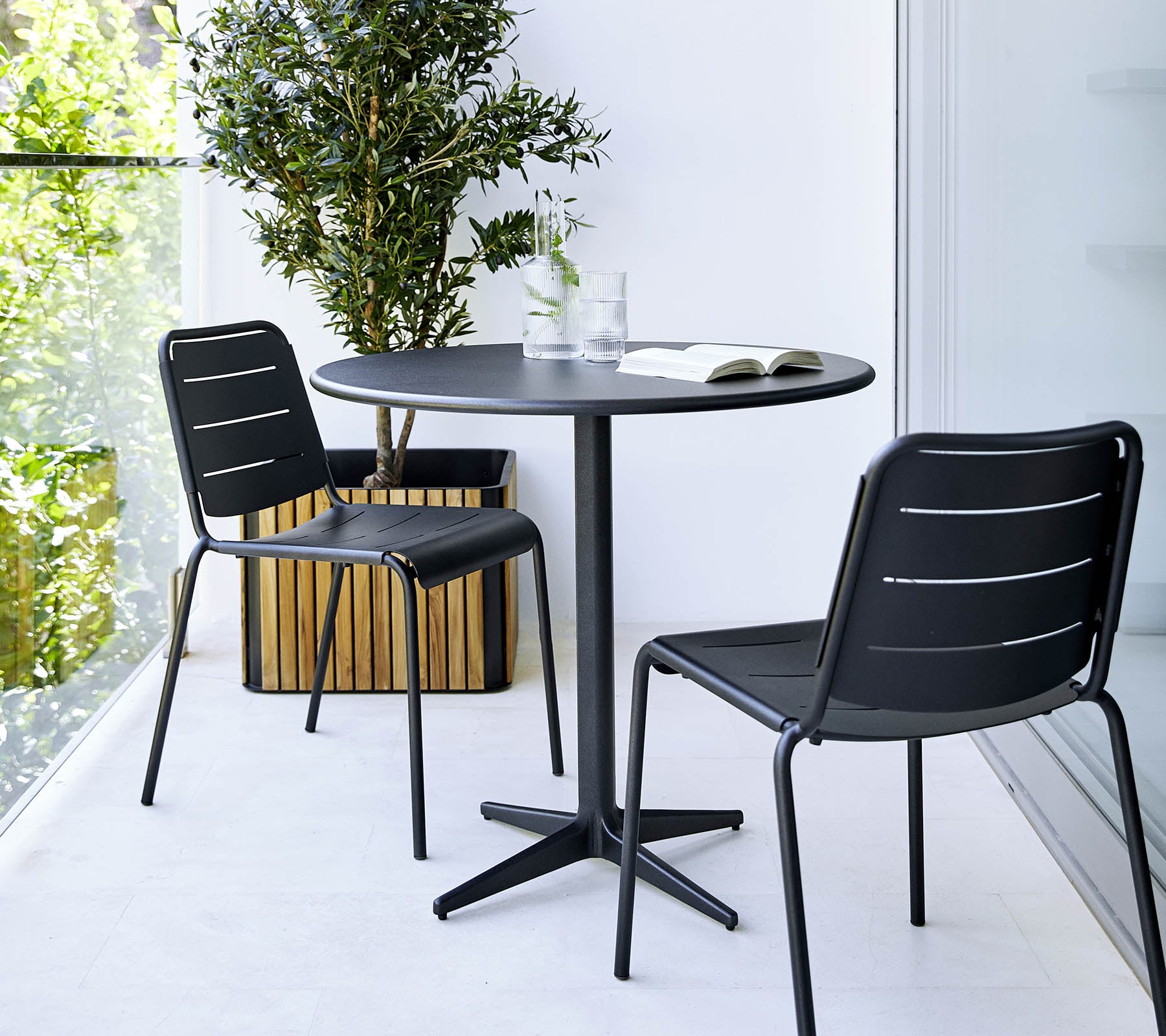 Klein rond tafel met twee zwarte stoelen en een potplant in de buurt, wat een minimalistische en stijlvolle setting creëert.