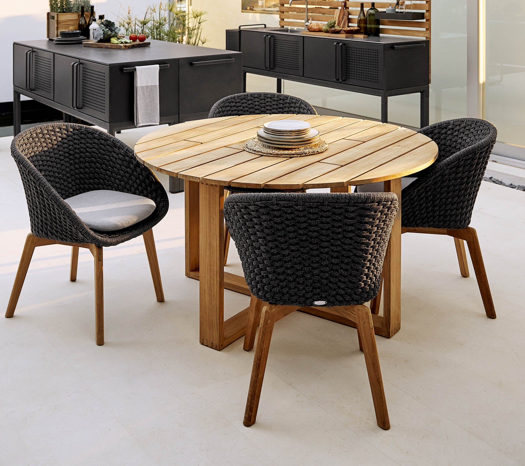 Ronde houten tafel met vier stijlvolle gevlochten stoelen, perfect voor diners en sociale bijeenkomsten. Elegante en uitnodigende buitenzitarrangement.