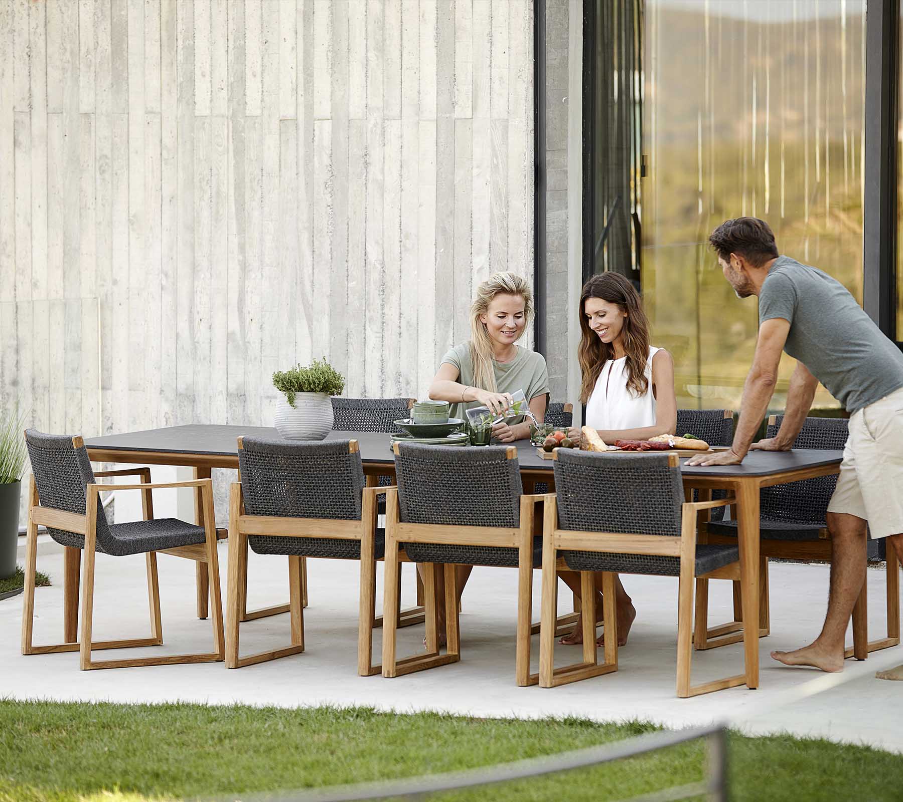 Vier mensen genieten samen van een maaltijd aan een stijlvolle houten eettafel, met moderne stoelen en een rustige buitenomgeving.