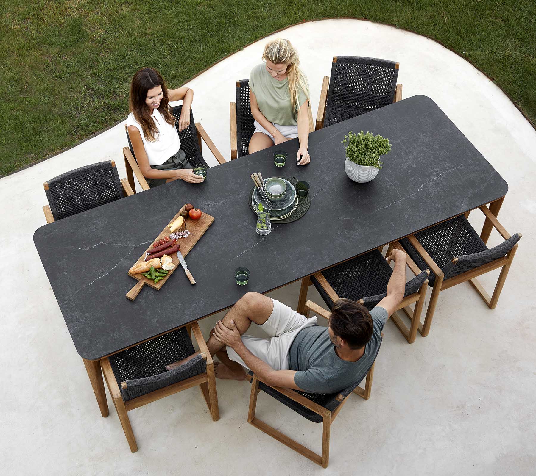Een groep mensen geniet van een maaltijd rond een grote tafel, met schalen, drankjes en een planten-centraalstuk. Informele eet-sfeer.