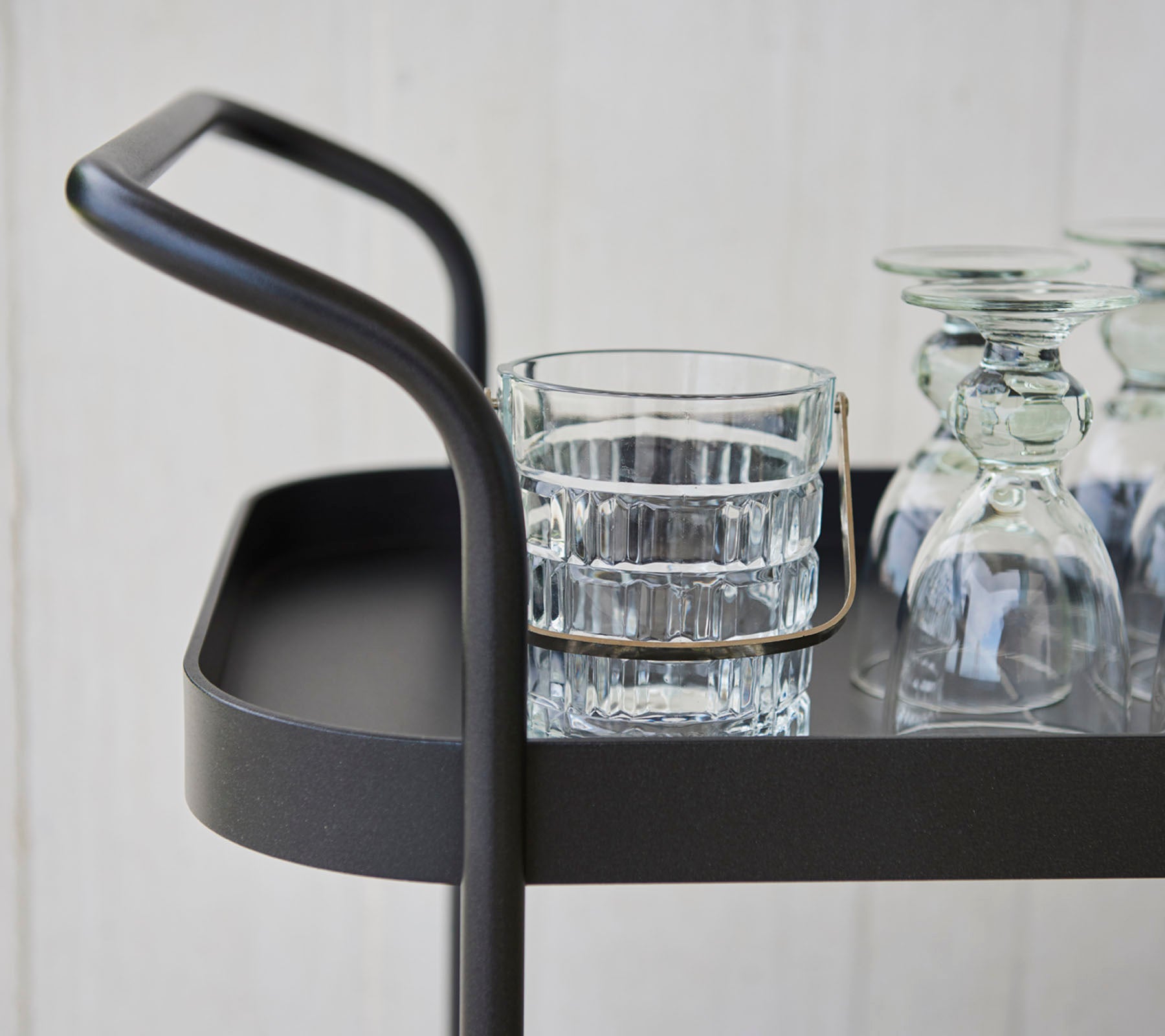 Stijlvolle serveerwagen met een slank handvat, met een glas tumbler en verschillende heldere glazen op een vlakke ondergrond.