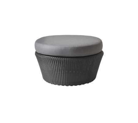 Rond ottoman met een geweven basis en een grijze, gewatteerde bovenkant, ontworpen voor veelzijdig zitten en decoratie.