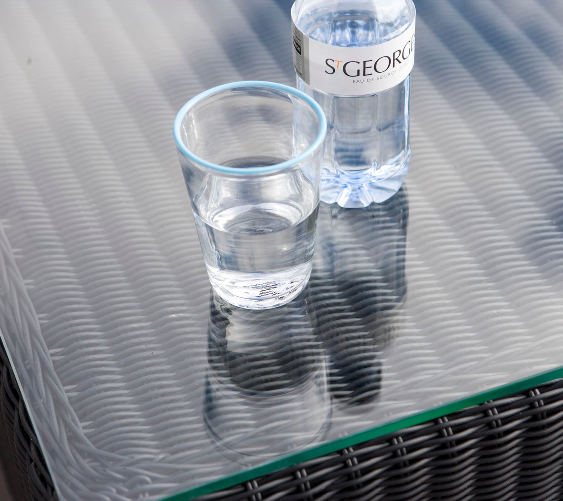 Een helder glas met water naast een waterfles op een gestructureerd tafeloppervlak.