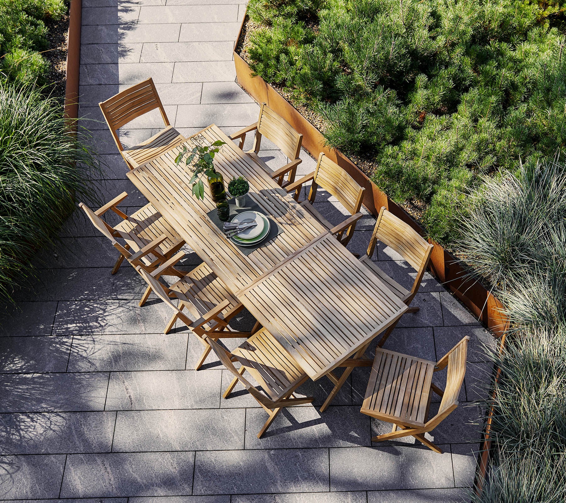 Een ruime houten eettafel omringd door bijpassende stoelen, versierd met een middelpunt en omlijst door weelderig groen.