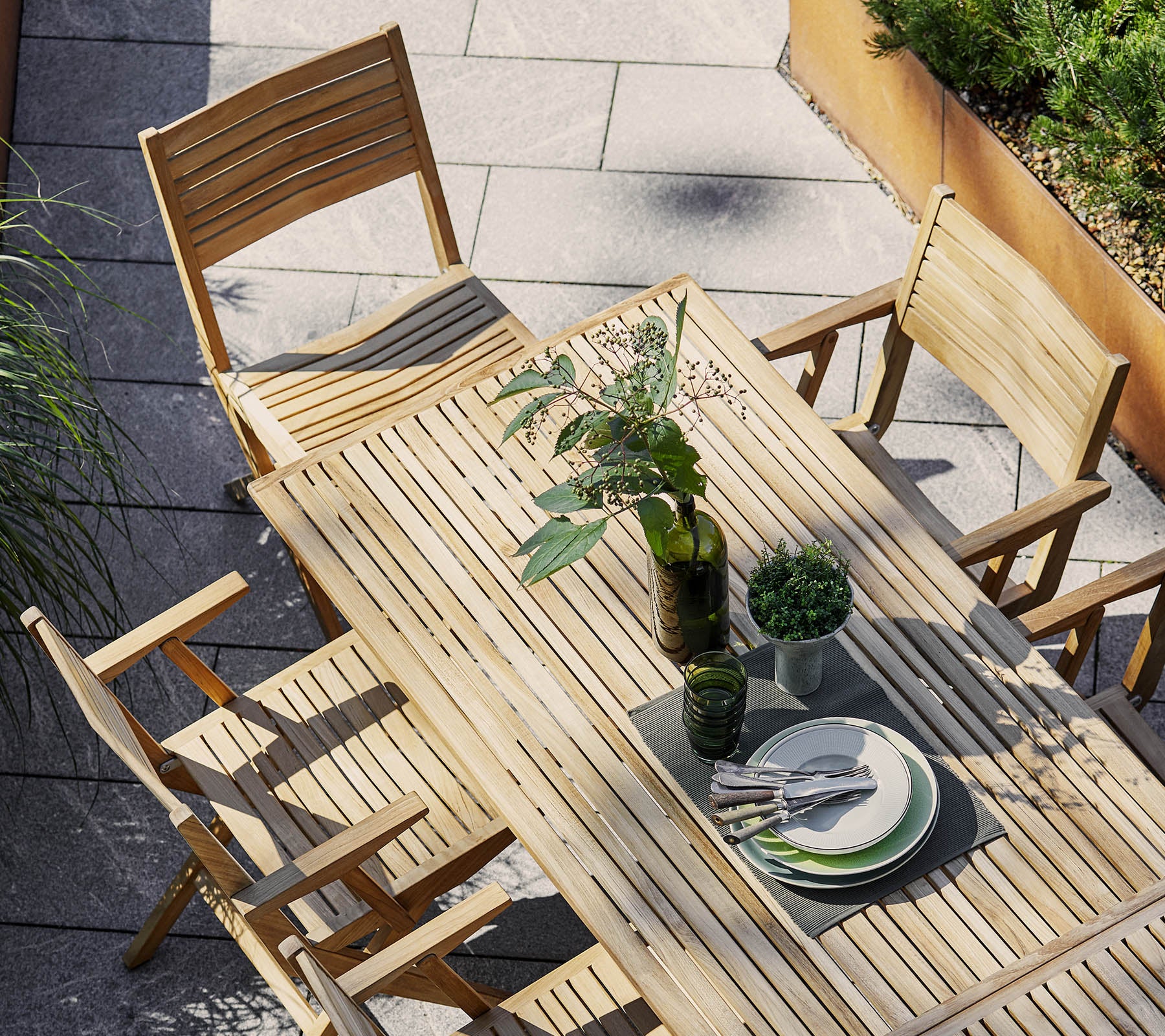 Houten eettafelset met een rechthoekige tafel en opvouwbare stoelen, versierd met groen en servies voor een uitnodigende sfeer.